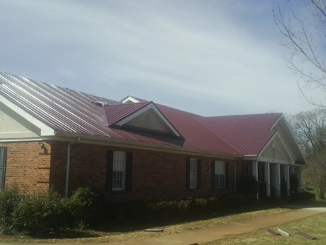 Red metal roof with gabled entries on a long brick building, from a Hail Damage Roof Repair job in Bogalusa