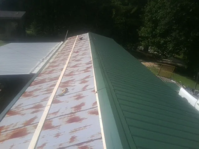 Old rusted panels beside newly installed green metal roofing — Wind Damage Roof Repair by Roofing Brothers in Bogalusa