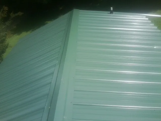 New green metal panels meeting at the ridge of a roof — Flat Roof Repair work by our crew in Bogalusa