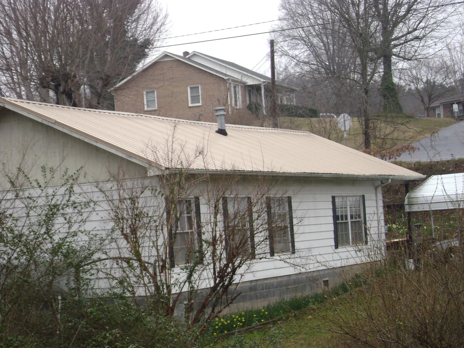 Tan metal roof on a white sided house set into a hillside — Commercial Roofing by Roofing Brothers in Bogalusa