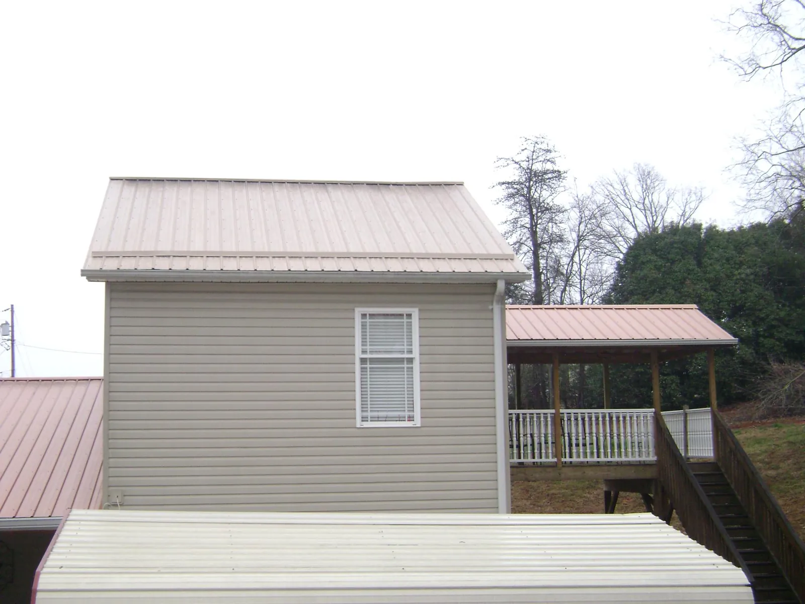 Tan metal roofs on a two story addition and attached porch, from a Roof Replacement job in Bogalusa